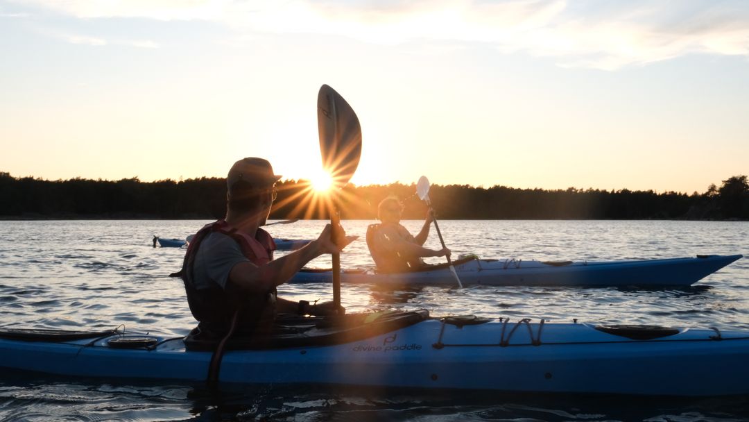 Zwei Seekajaks auf stillem Wasser, die Abendsonne steht tief hinter einem erhobenen Paddel
